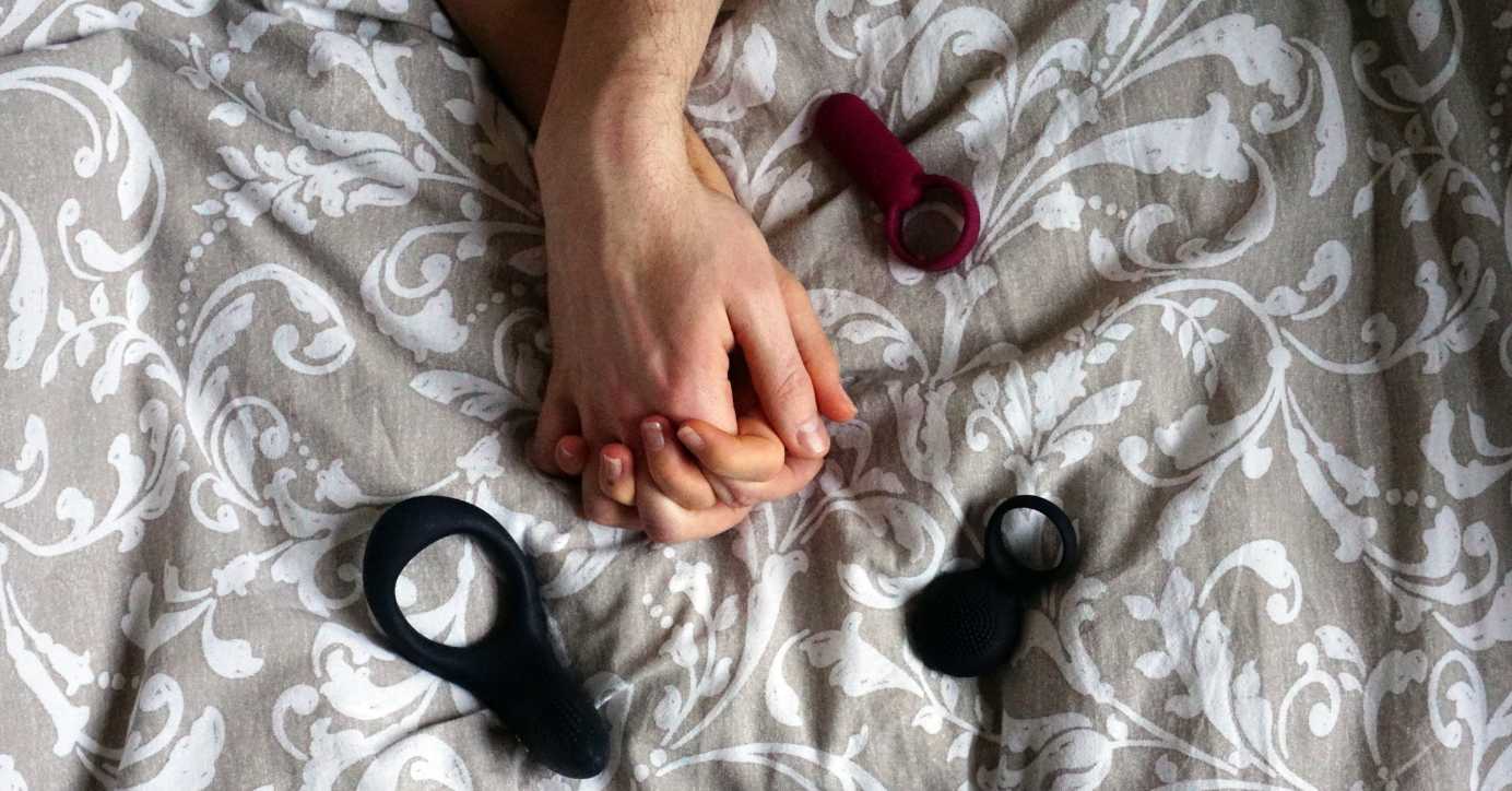 Paar hält Händchen auf Bett mit Partnervibratoren und Erotikspielzeug