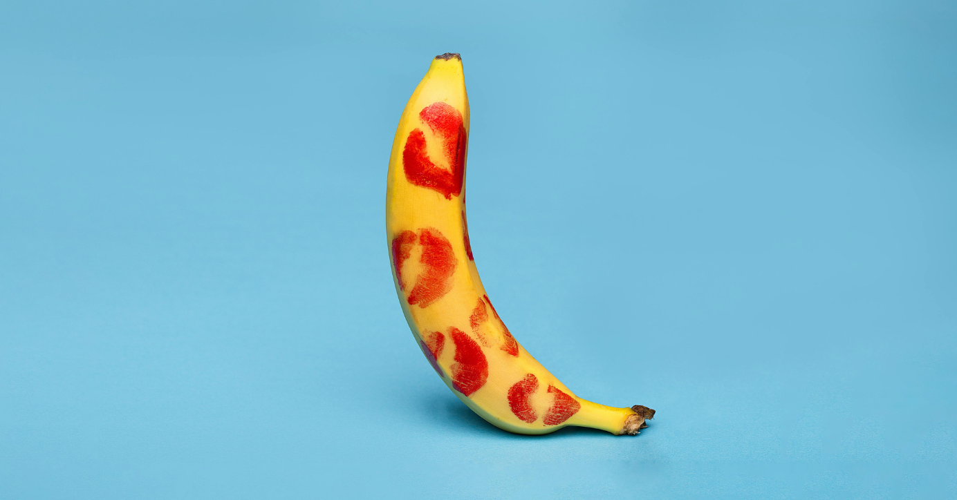 Banane mit roten Lippenstift-Kussabdrücken auf blauem Hintergrund, Symbol für Erotik und Liebesspiel