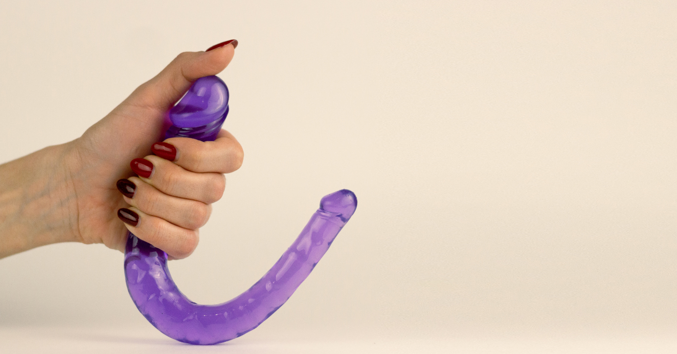 Hand hält lila Dildo, Nahaufnahme, Sexspielzeug für Erwachsene vor hellem Hintergrund