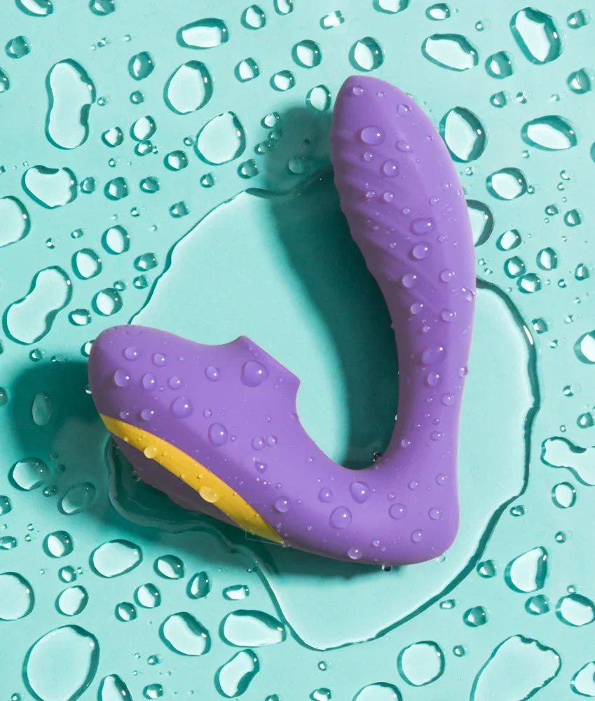 Lila wasserdichter Vibrator mit gelbem Detail, umgeben von Wassertropfen auf türkisem Untergrund