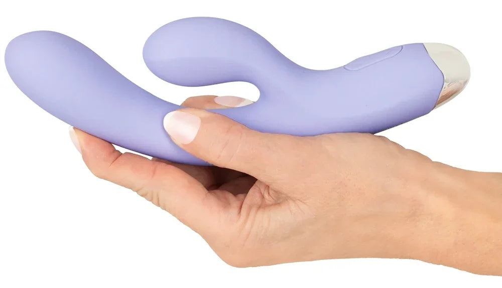 Lila Doppel-Vibrator mit Klitorisstimulator, gehalten in Hand – ideal für Paare & Solo