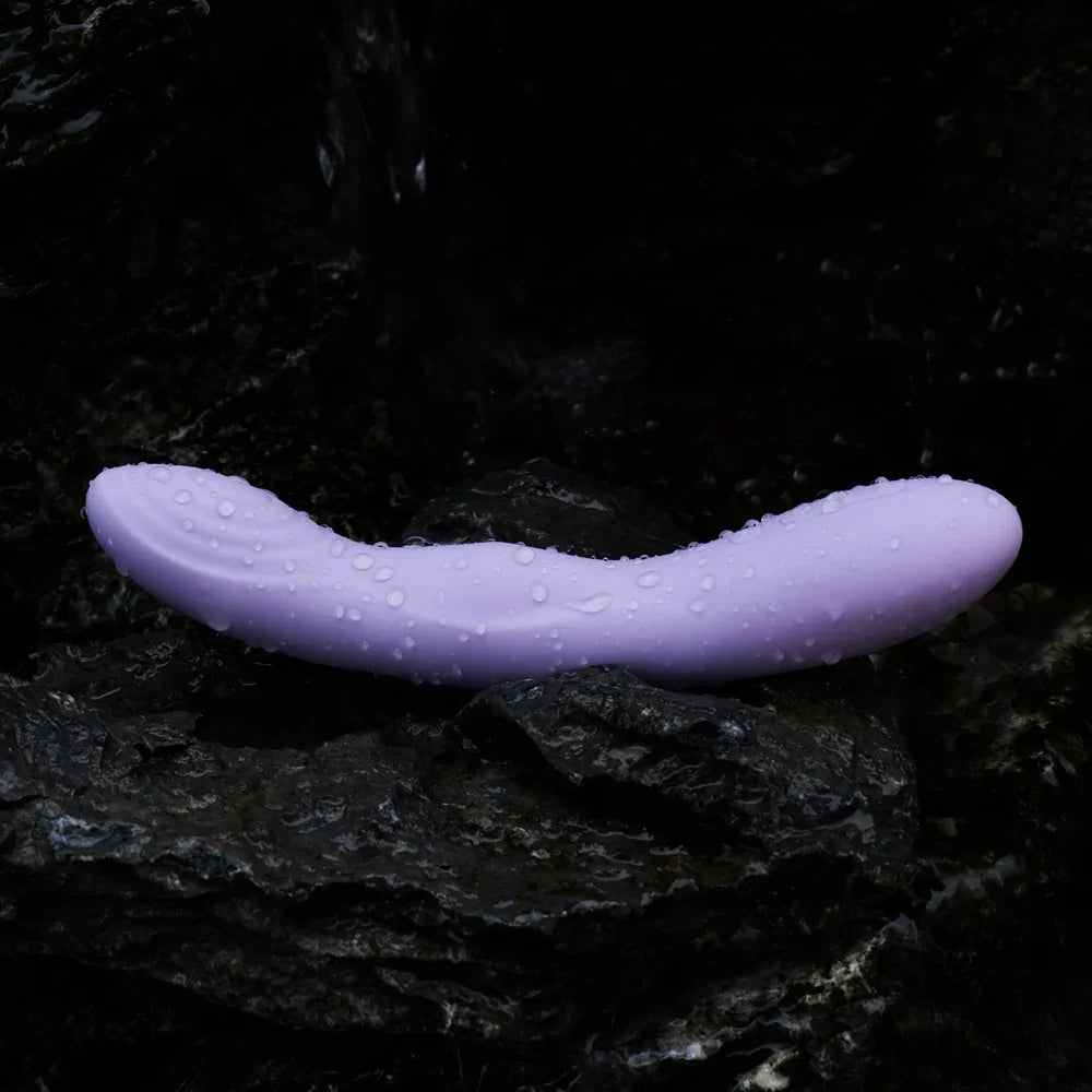 Lila Vibrator mit Wassertropfen auf dunklem Stein, wasserdicht für das Liebesleben