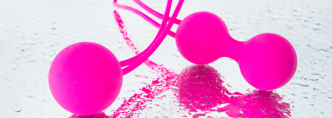 Zwei pinke Liebeskugeln aus Silikon auf nasser Oberfläche, Erotikspielzeug Produktfoto