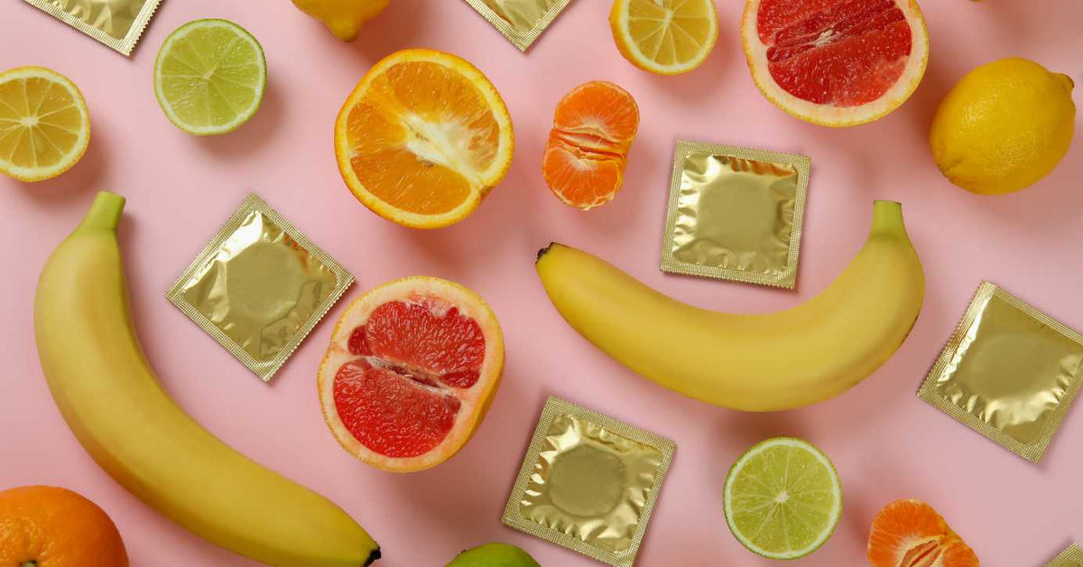 Bananen, Zitrusfrüchte und goldene Kondomverpackungen auf rosa Hintergrund, Sexualität, Verhütung