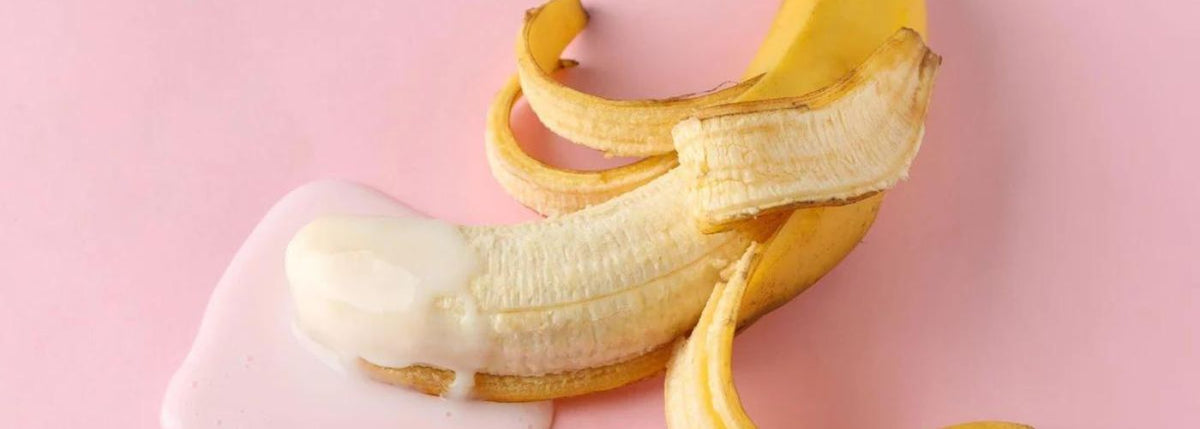 Halb geschälte Banane mit weißem Gleitgel auf rosa Hintergrund, Symbolbild für Sexspielzeug.