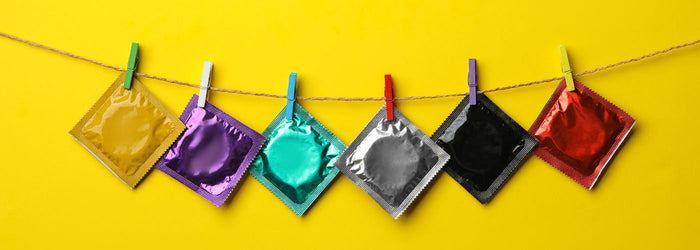 Bunte Kondomverpackungen hängen an Wäscheleine vor gelbem Hintergrund, Erotikartikel