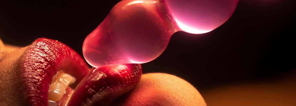 Rote Lippen berühren rosafarbenen Silikon-Vibrator im erotischen Nahaufnahme-Sexshop-Kontext