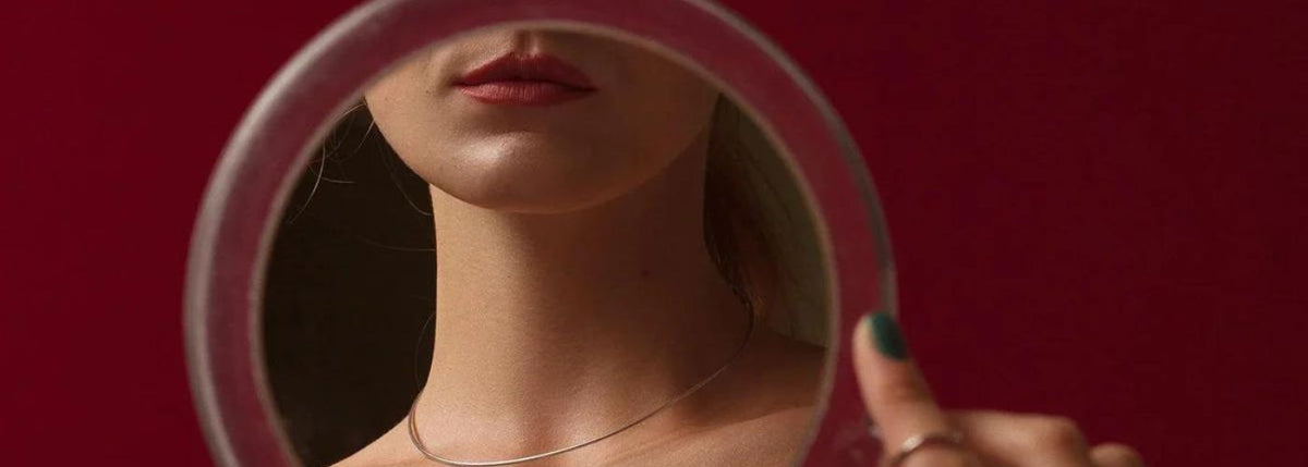 Sinnliche Frau betrachtet sich im Spiegel, rote Lippen, erotische Stimmung, roter Hintergrund