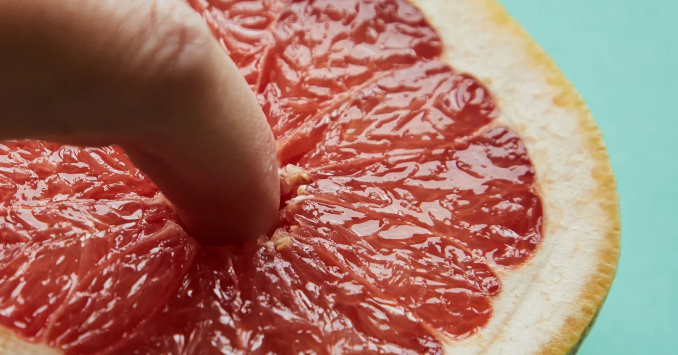 Nahaufnahme: Finger berührt halbierte Grapefruit, symbolisch für Lust, Erotik, Intimität