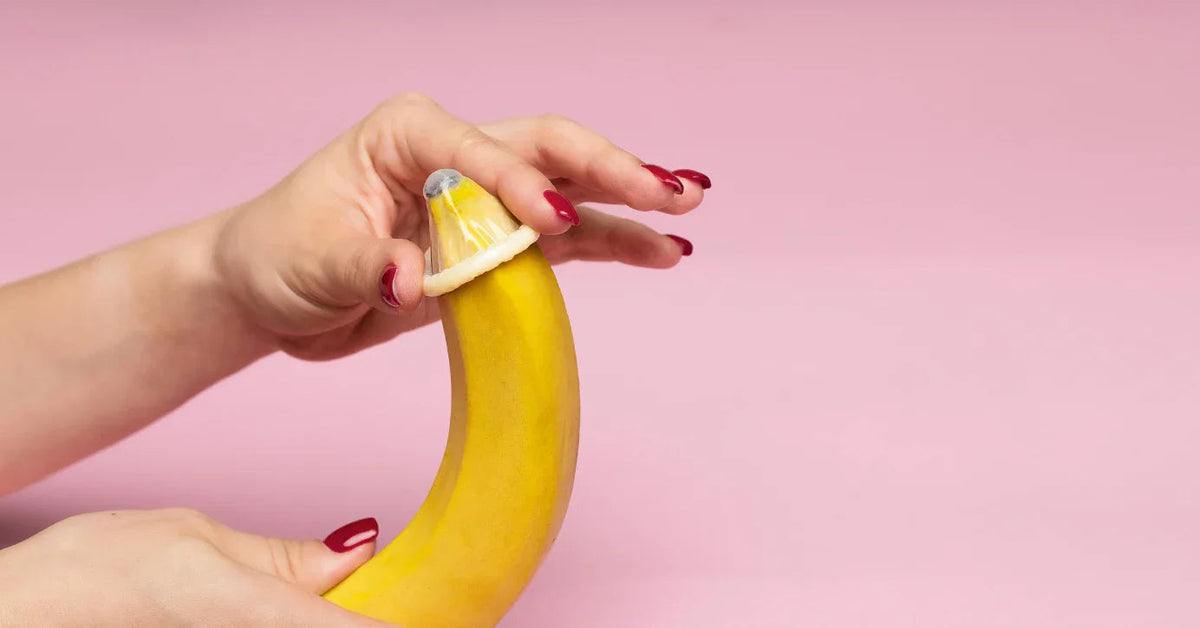 Hand mit roten Nägeln zieht Kondom über Banane, Sexualaufklärung, safer Sex Symbol