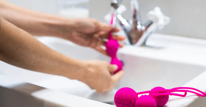 Hand reinigt pinke Liebeskugeln aus Silikon am Waschbecken, Sexspielzeug Pflege