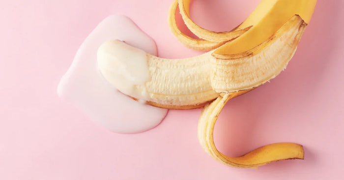 Halb geschälte Banane mit weißem Gleitmittel auf rosa Hintergrund, Symbol für Lust und Erotik.