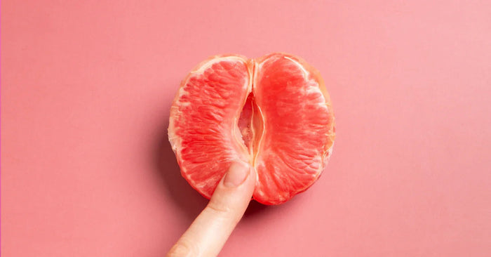 Halbe Grapefruit mit Finger auf rosa Hintergrund, Symbol für weibliche Sexualität und Aufklärung