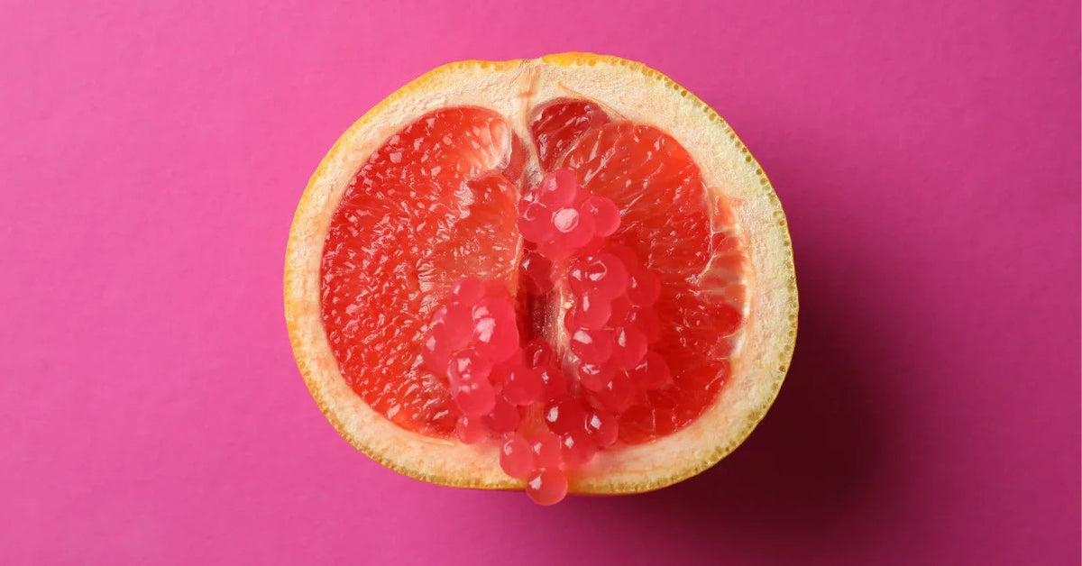 Halbe Grapefruit mit rosafarbenen Kugeln auf pinkem Hintergrund als Symbol für Lust und Erotik