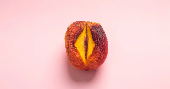 Halbierte, reife Pfirsich auf rosa Hintergrund, Symbolbild für Sexualität und Intimität