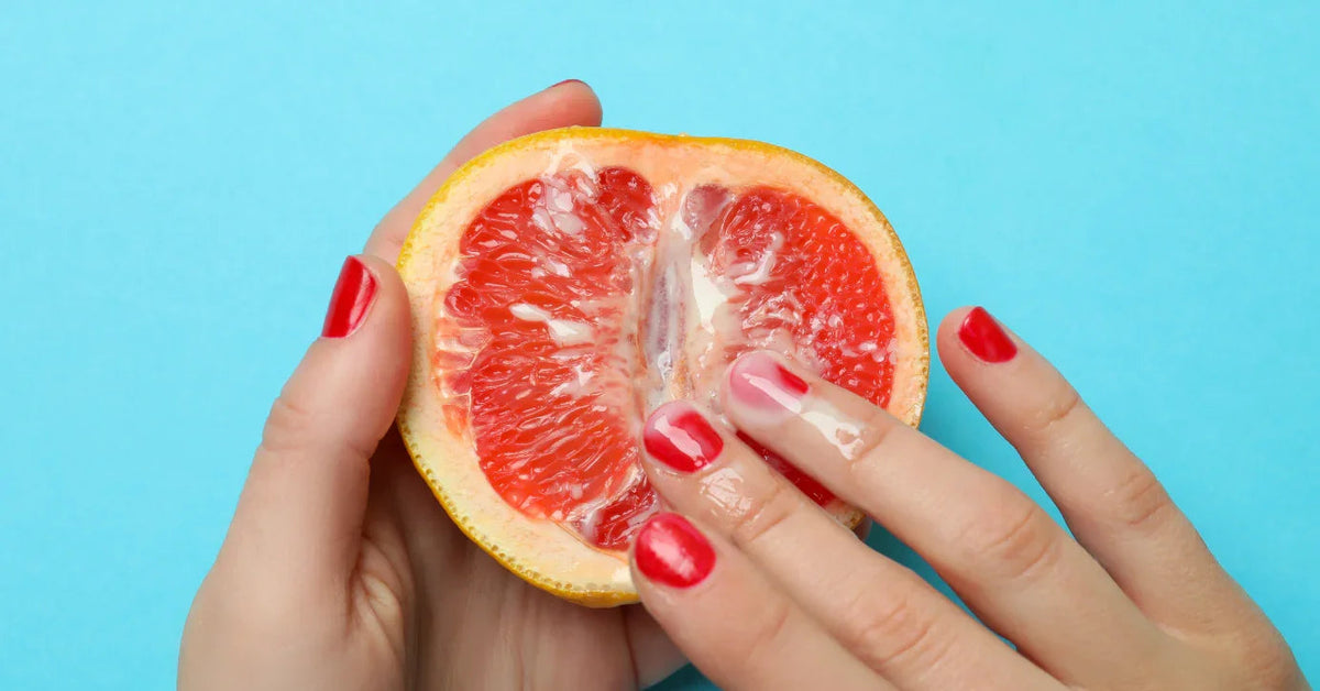 Hand mit rotem Nagellack berührt saftige Grapefruit mit Gleitgel auf blauem Hintergrund