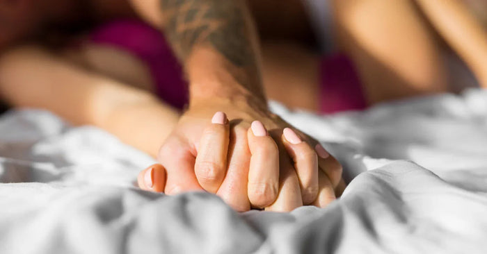 Zwei Personen halten sich leidenschaftlich an der Hand im Bett, Symbol für Intimität und Erotik
