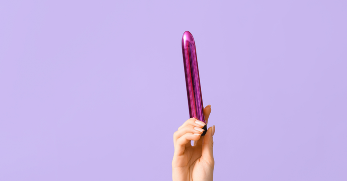 Hand hält lila Vibrator, Erotikspielzeug vor lila Hintergrund, Diskretes Sextoy-Foto