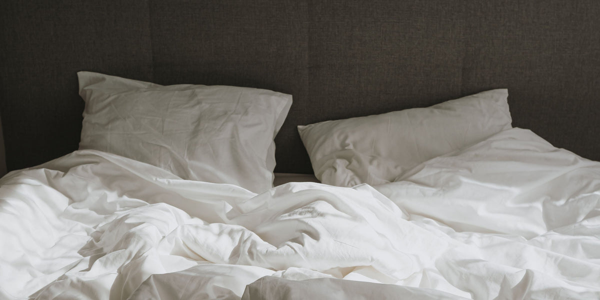 Unordentliches Bett mit weißen Kissen und Decken, Symbol für intimes Liebesleben