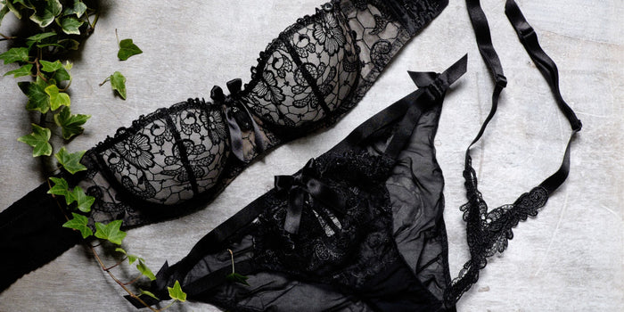 Schwarzes Spitzen-Dessous-Set mit BH und Slip, erotisch und sinnlich auf Holz mit Efeu