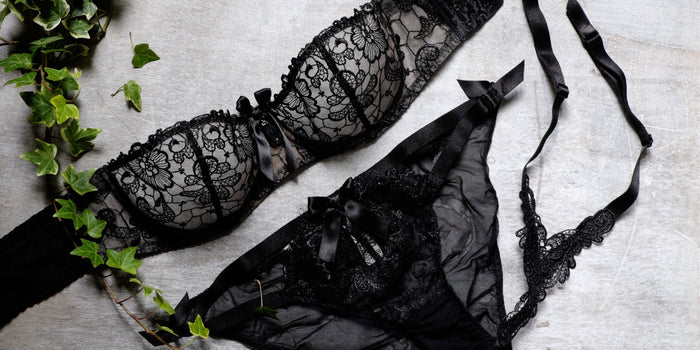 Schwarzes Spitzen Dessous-Set mit BH und Slip auf grauem Hintergrund, sinnliche Unterwäsche