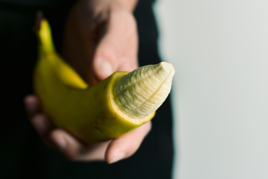 Hand hält halbgeschälte Banane als Symbol für Erotik, Sexualität, Liebesleben