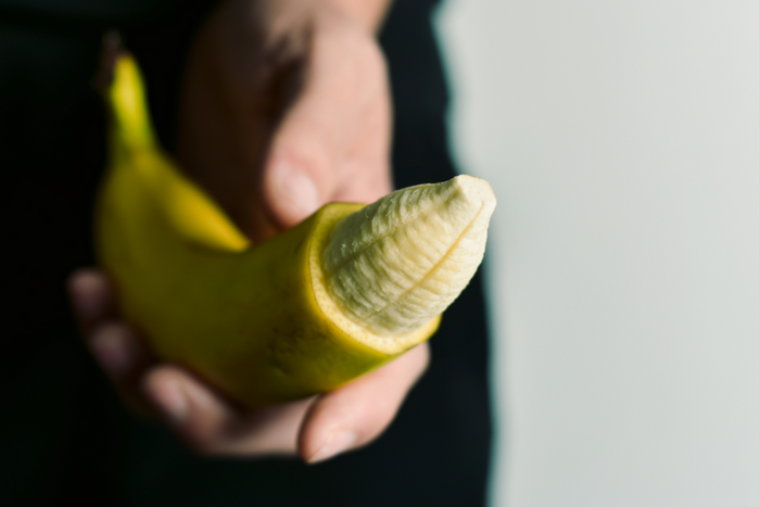 Hand hält halbgeschälte Banane als Symbol für Erotik, Sexualität, Liebesleben