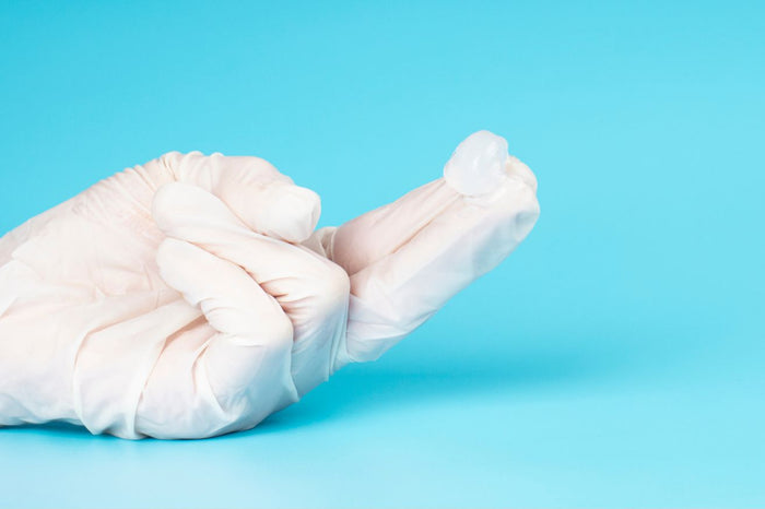 Hand mit Handschuh hält Gleitgel auf Finger vor blauem Hintergrund, Sexualzubehör