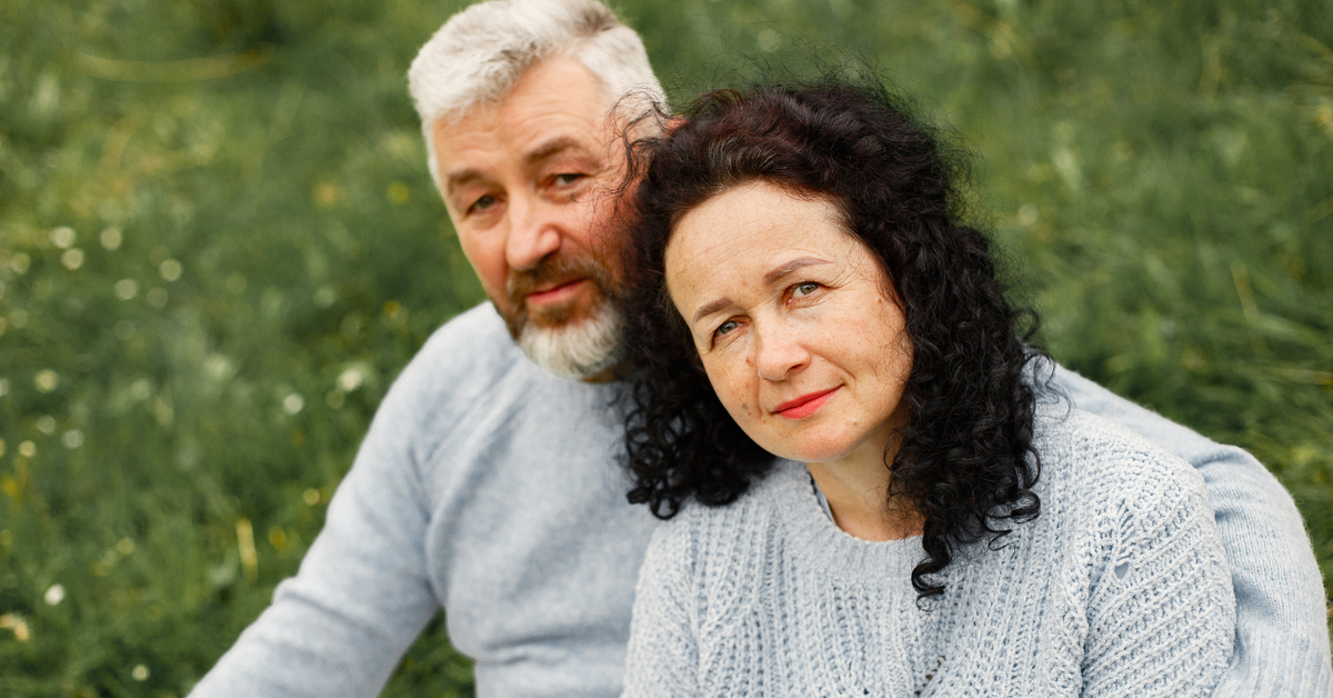 Älteres Paar sitzt eng zusammen im Grünen und trägt hellblaue Pullover, Nähe und Vertrauen