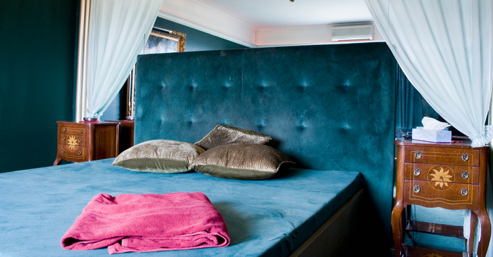 Modernes Schlafzimmer mit Himmelbett, samtigem Kopfteil, Zierkissen und rotem Handtuch, diskrete Atmosphäre für intime Momente