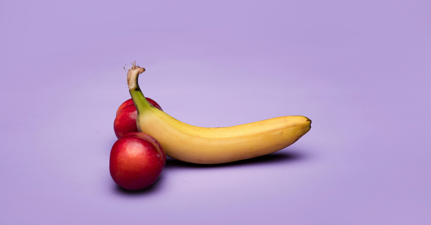 Banane und zwei rote Pflaumen auf lila Hintergrund, symbolisieren Erotik und Lust