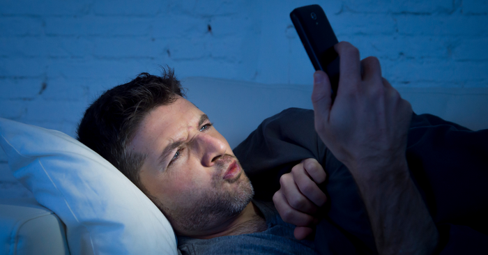 Mann liegt abends im Bett und schaut neugierig auf sein Smartphone, diskrete Erotikshop-Szene