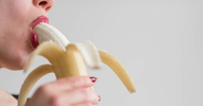 Nahaufnahme einer Frau mit rotem Lippenstift, die eine Banane mit erotischer Geste isst