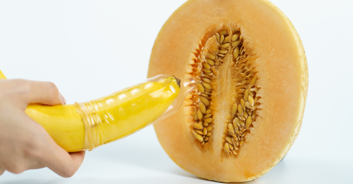 Banane mit Kondom vor halbierter Honigmelone, Symbol für Safer Sex und Verhütung