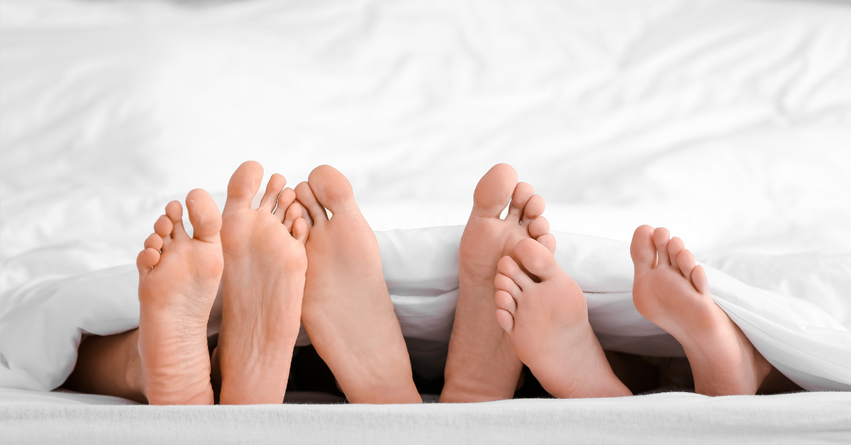 Vier Füße eines Paares unter einer weißen Bettdecke, Symbol für Intimität und Liebesleben