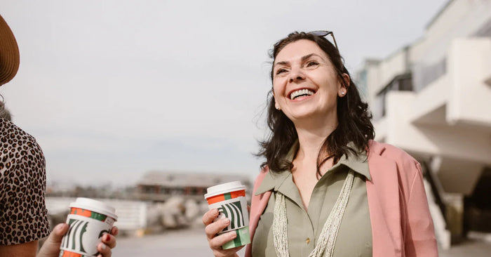 Lächelnde Frau im Freien mit Kaffeebecher, freundliches Gespräch, Alltagsszene