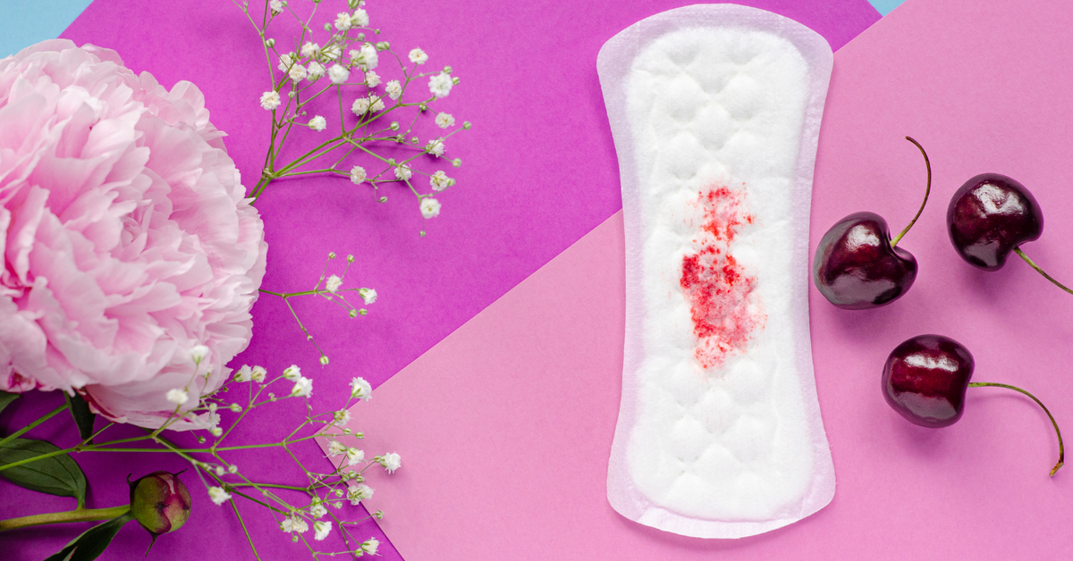 Binde mit Blutfleck auf buntem Hintergrund, daneben Blüten und Kirschen, Symbol für Menstruation.