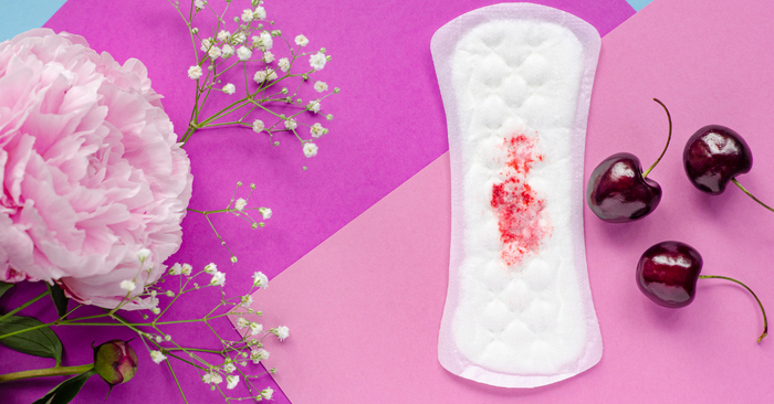 Binde mit Blutfleck auf buntem Hintergrund, daneben Blüten und Kirschen, Symbol für Menstruation.