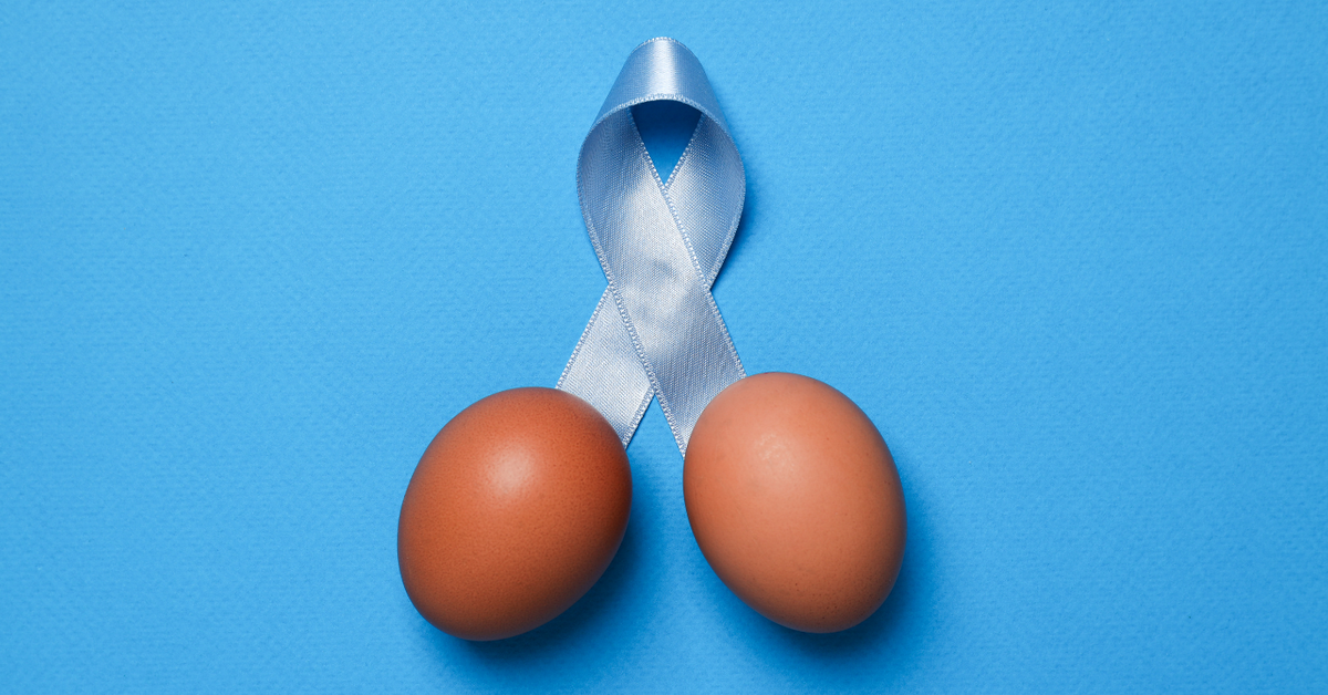 Zwei braune Eier und eine hellblaue Schleife auf blauem Hintergrund, Symbol für Männergesundheit, Sexualwohlbefinden