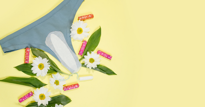 Slip mit Slipeinlage, Tampons und Blumen auf gelbem Hintergrund, Hygieneprodukte für Frauen
