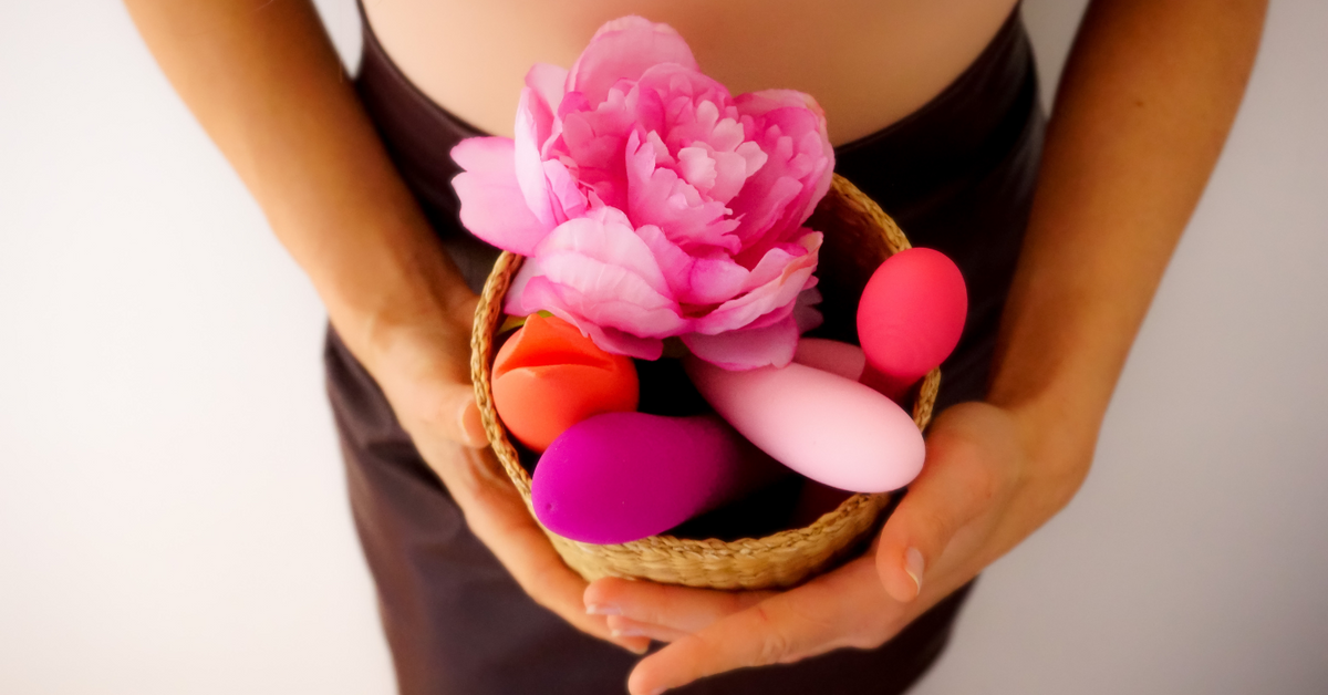 Frau hält Korb mit bunten Vibratoren und rosa Blume, Erotikartikel, intime Accessoires