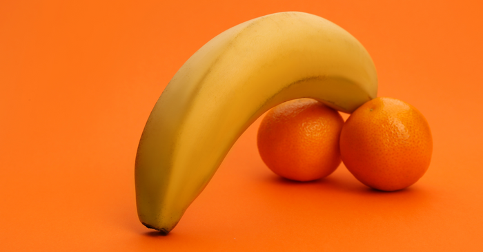 Banane und zwei Mandarinen auf orangefarbenem Hintergrund, symbolisch für Erotik und Liebesspiele