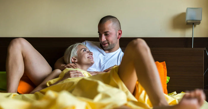 Paar liegt intim lächelnd im Bett unter gelber Decke, Sinnlichkeit und Zweisamkeit
