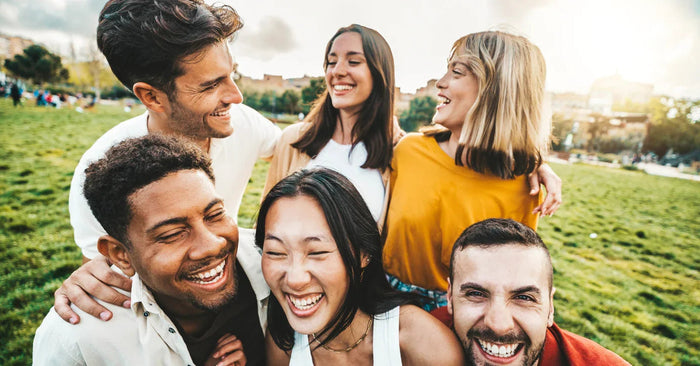 Gruppe von jungen Menschen, die glücklich und ausgelassen im Park gemeinsam lachen, Vielfalt, Freundschaft, positive Stimmung