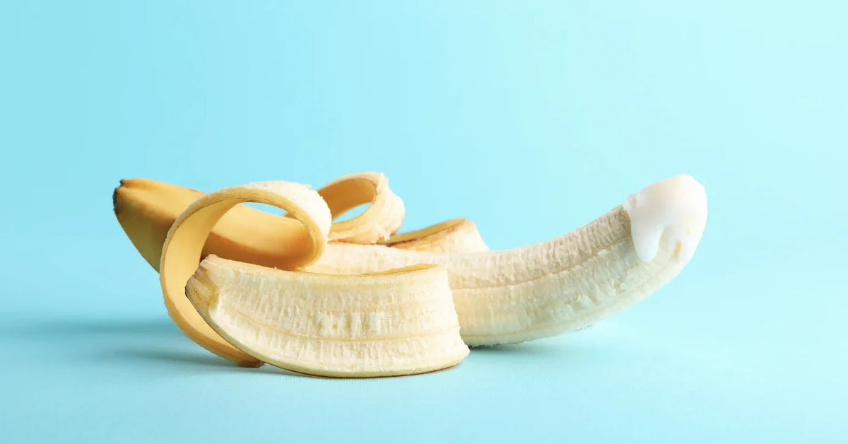 Halb geschälte Banane mit Creme auf der Spitze als erotische Andeutung auf blauem Hintergrund