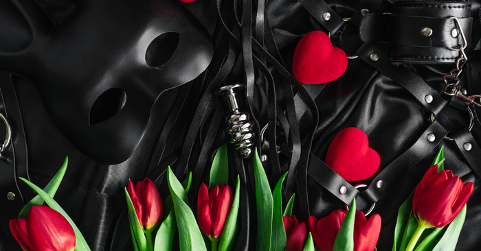 Erotische Accessoires, Masken, Handschellen, Peitsche und rote Tulpen auf schwarzem Satin