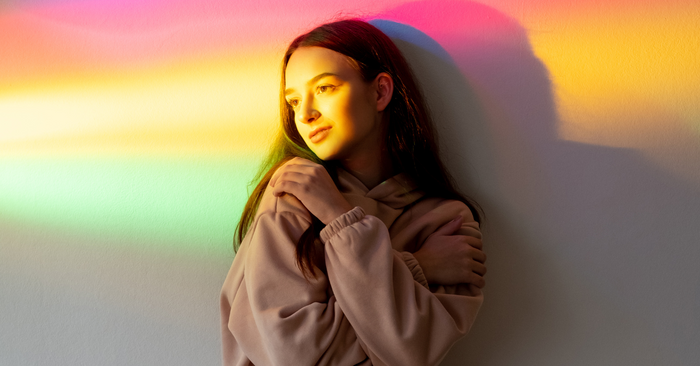 Frau vor Wand mit Regenbogenlicht, Symbol für Vielfalt, Erotik und Selbstliebe